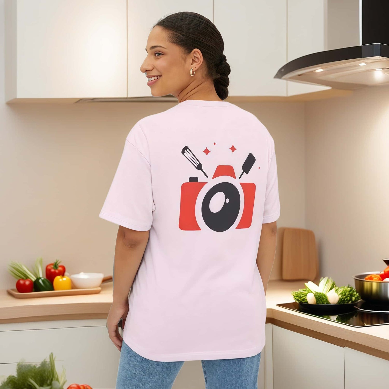 Woman standing in a modern kitchen displaying a pink t-shirt with our company logo affixed